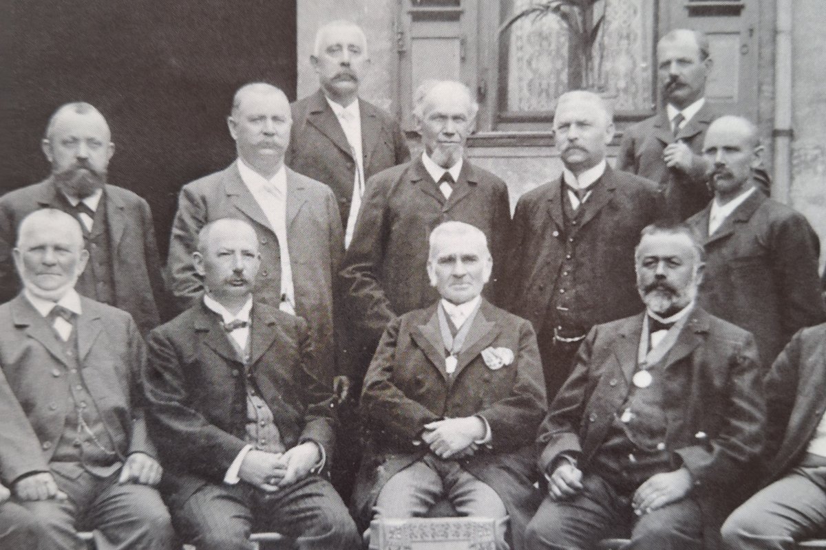 Historisches Gruppenfoto von zwölf Männern vor einer Hausfassade: Wilhelm Hermann Diehl sitzt in der vorderen Reihe als zweite Person von links.