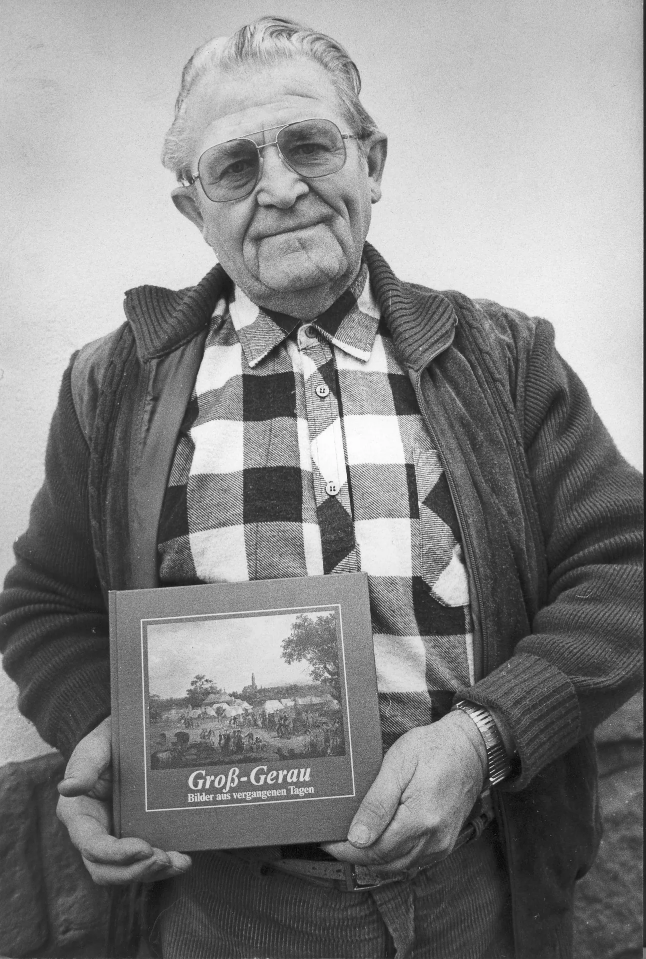 Schwarzweiß-Porträt von Ernst Schneider, der das von ihm herausgegebene Buch „Groß-Gerau – Bilder aus vergangenen Tagen“ in den Händen hält.